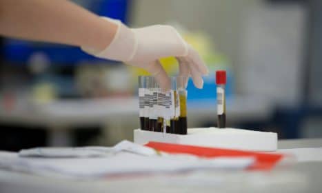 A person in white gloves is putting a bottle of wine in a test tube