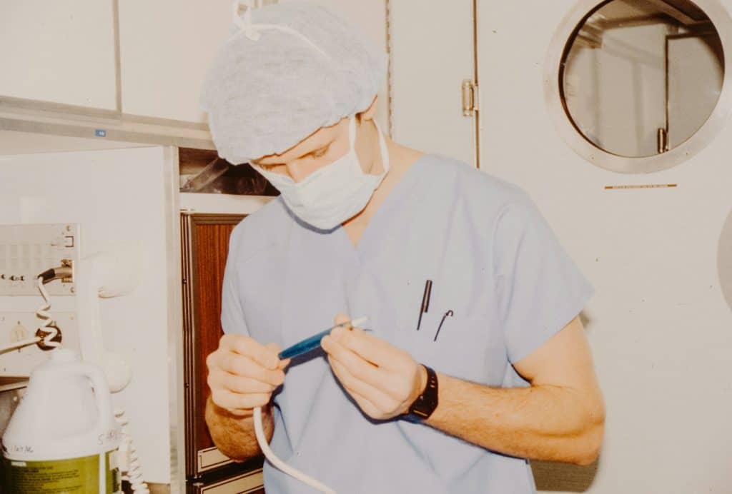 A surgeon in scrubs and mask prepares equipment.