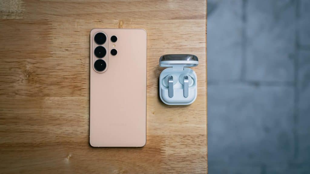 Peach smartphone and wireless earbuds on wooden table