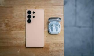 Peach smartphone and wireless earbuds on wooden table