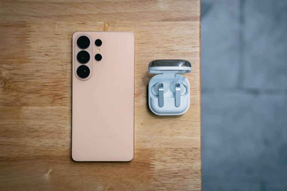 Peach smartphone and wireless earbuds on wooden table