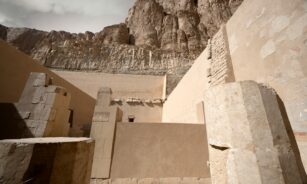 Ancient egyptian temple ruins with rocky cliffs above.