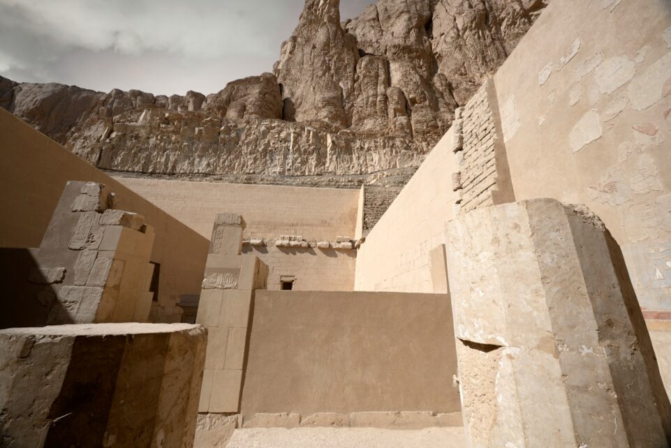 Ancient egyptian temple ruins with rocky cliffs above.