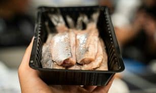 person holding black plastic tray with meat