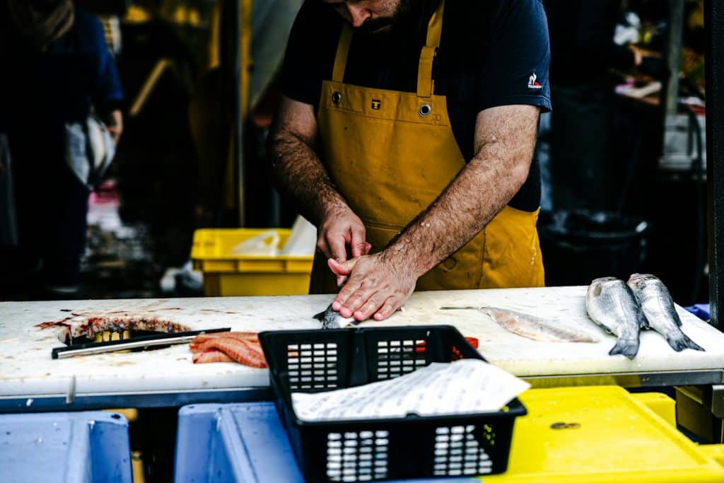 A man in an apron prepares fish on a table.