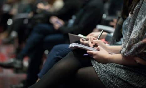 selective focus photography of people sitting on chairs while writing on notebooks