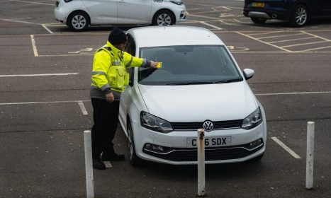 man in yellow jacket standing beside white car