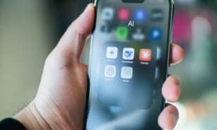 A hand holds a smartphone with various apps.