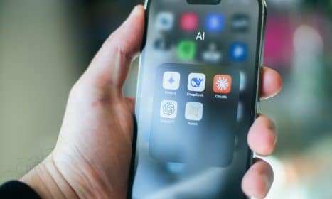 A hand holds a smartphone with various apps.