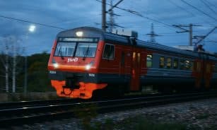 Red and grey train moving on tracks at dusk.