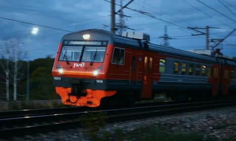 Red and grey train moving on tracks at dusk.