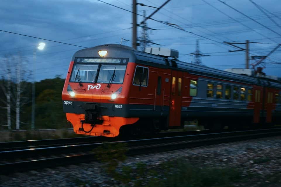 Red and grey train moving on tracks at dusk.