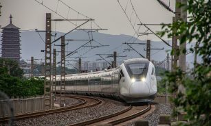 a white train traveling down train tracks next to a forest