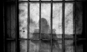 a shadow of a person behind bars in a jail cell