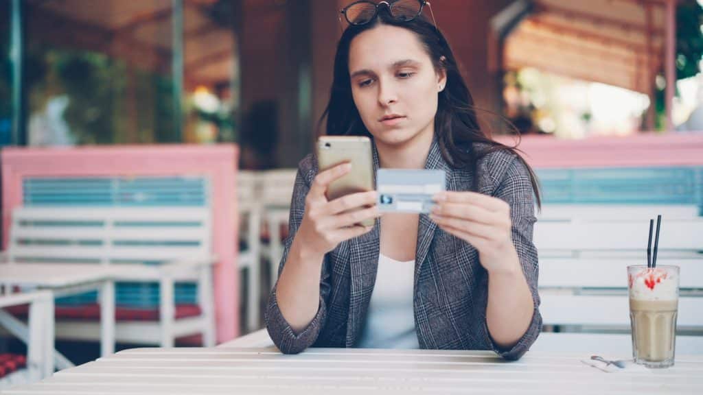 Woman holding credit card and phone at cafe