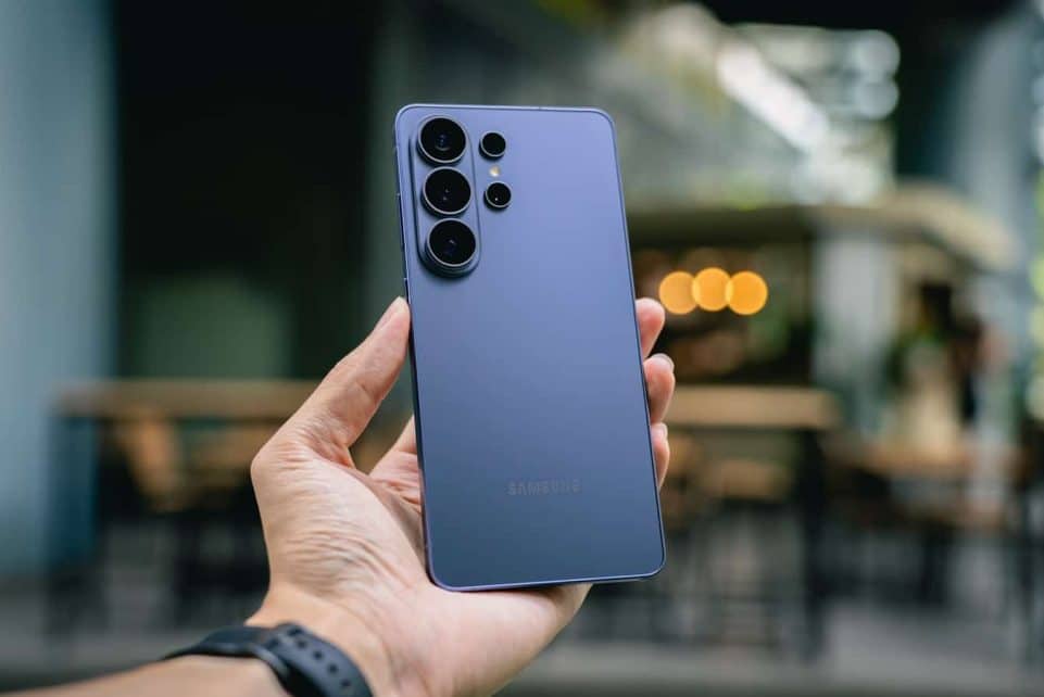 Hand holding a blue smartphone with multiple cameras.