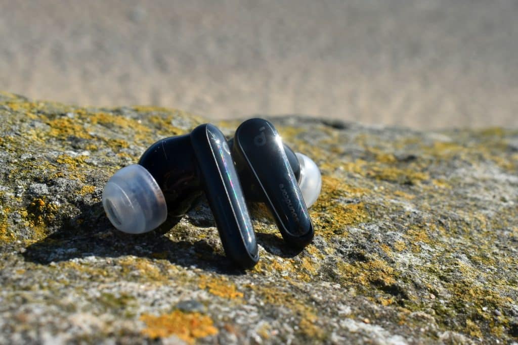 Black wireless earbuds resting on a textured rock.