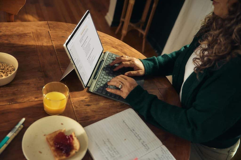 Woman typing on laptop at wooden table with breakfast.