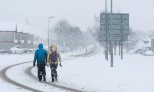 2 person walking on snow covered road during daytime