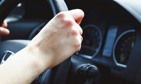 a person driving a car with their hand on the steering wheel
