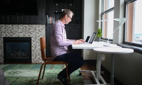man in gray dress shirt sitting on brown wooden chair using macbook pro