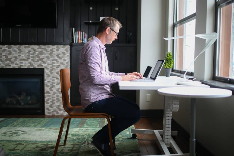 man in gray dress shirt sitting on brown wooden chair using macbook pro