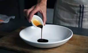 person dripping black liquid from small white ceramic bowl to big white ceramic bowl