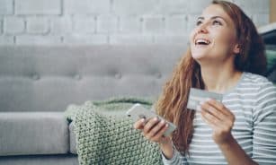 A happy woman holding a credit card and smartphone.