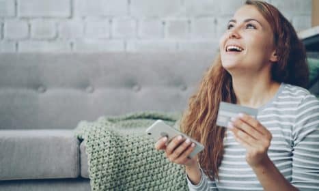 A happy woman holding a credit card and smartphone.