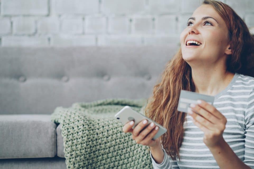A happy woman holding a credit card and smartphone.