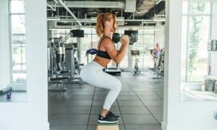 woman wearing black sports bra and white legging lifting dummbells