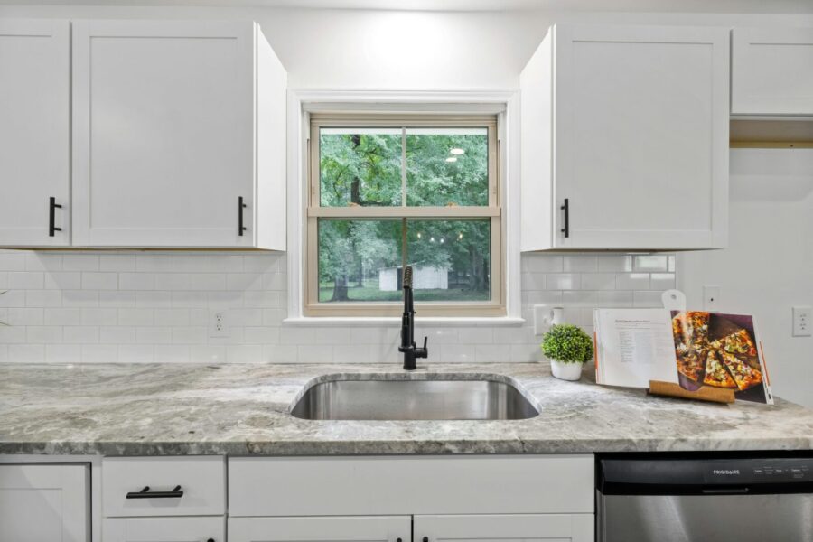 Bright kitchen interior featuring white cabinets, granite countertop, and a window with a view.