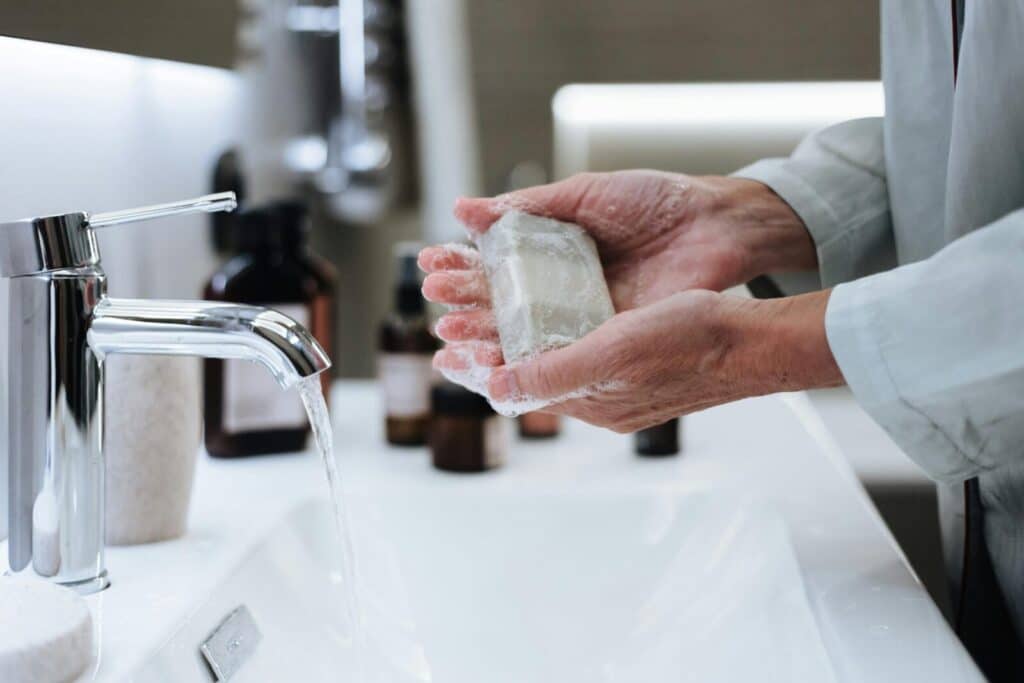 Hands washing with soap under running water in a modern bathroom setting.