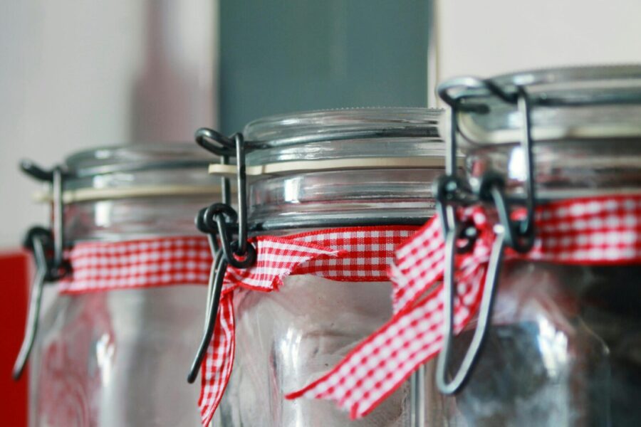 Three glass jars adorned with red gingham ribbons, ideal for kitchen storage or decoration concepts.