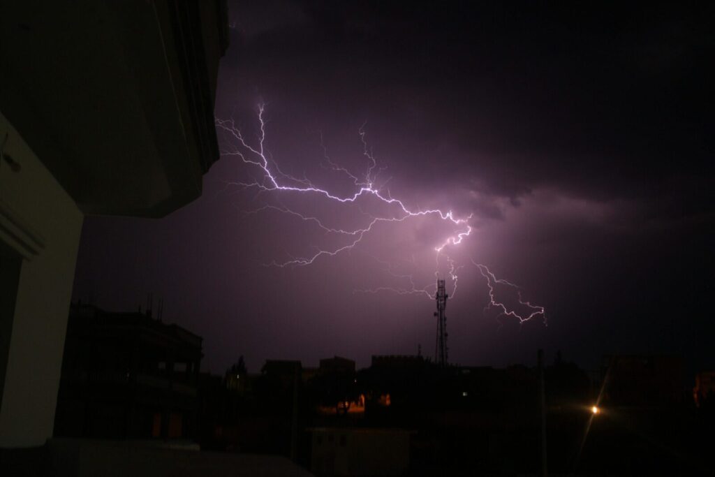 A striking lightning storm illuminates the night sky above silhouetted city buildings.