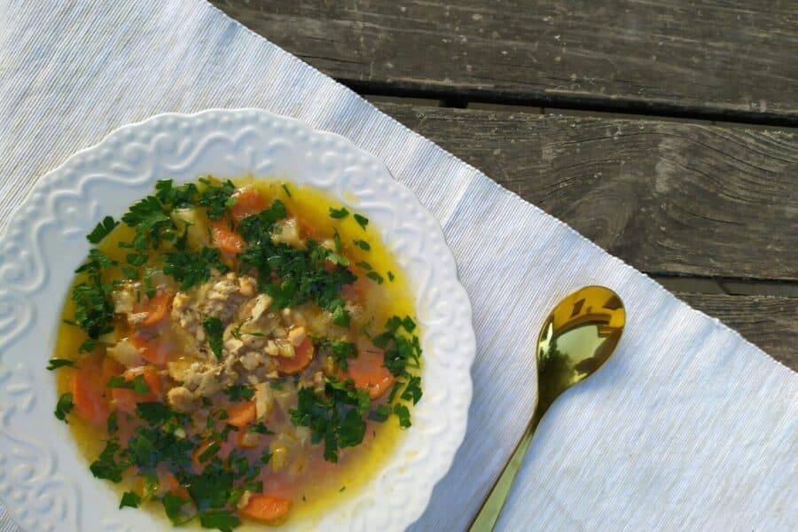 Delicious homemade chicken soup garnished with fresh parsley, served on a rustic table setting.