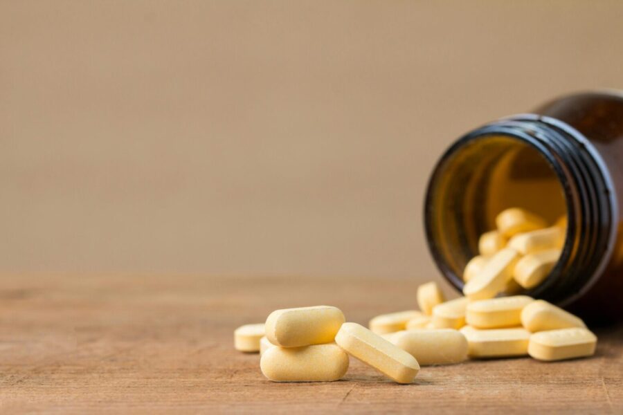 Yellow tablets spilling from an open brown glass bottle on a wooden surface, isolated on beige background.