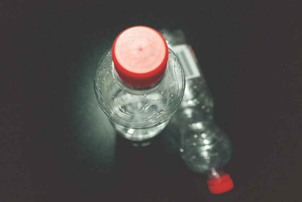 Top view of two clear plastic bottles with red caps on a dark surface, highlighting recycling.