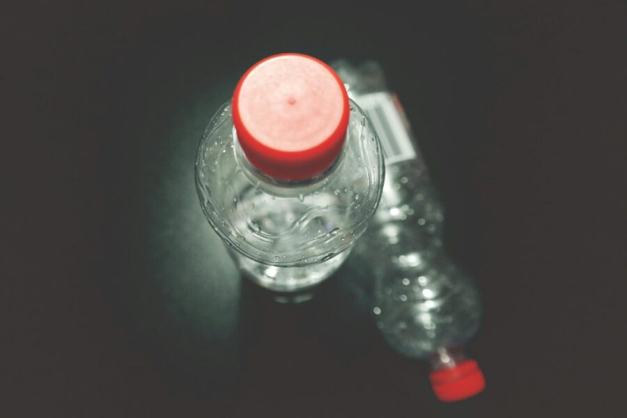 Top view of two clear plastic bottles with red caps on a dark surface, highlighting recycling.