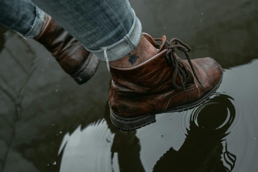 Brown leather boots stepping in a puddle with clear water reflection.