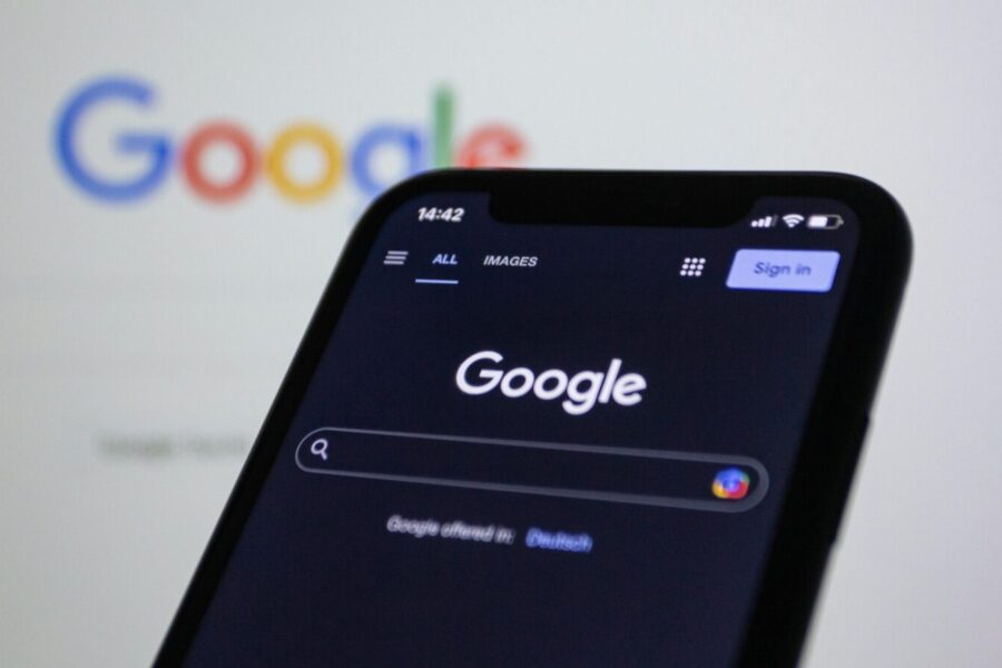 Smartphone screen showing Google search in dark mode with the Google logo in the background.