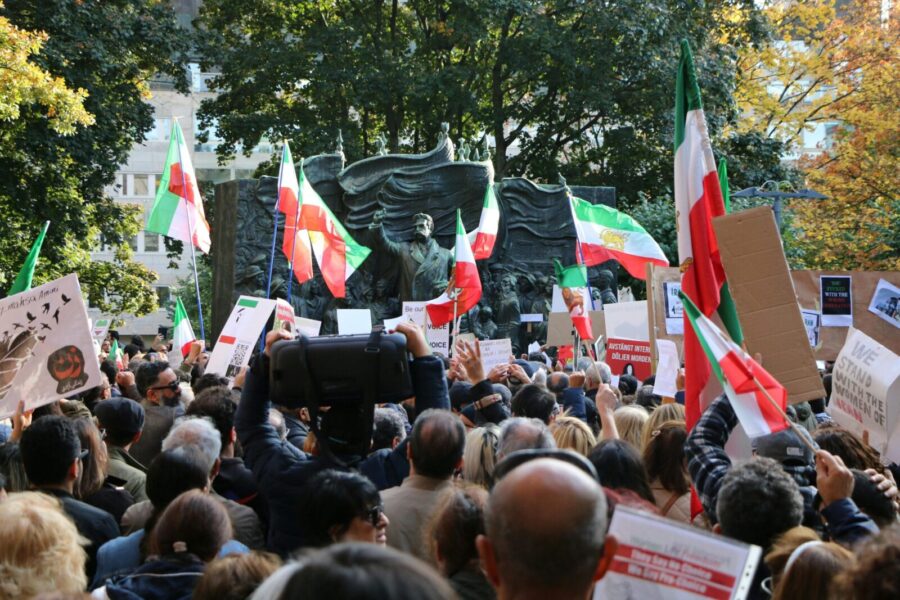 Protest gathering in central Stockholm featuring Iranian flags and banners.