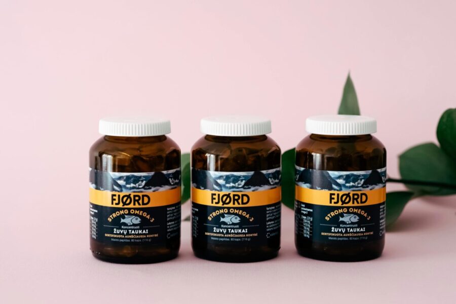 Three FJORD Omega-3 supplement bottles on a pink backdrop with greenery accents.
