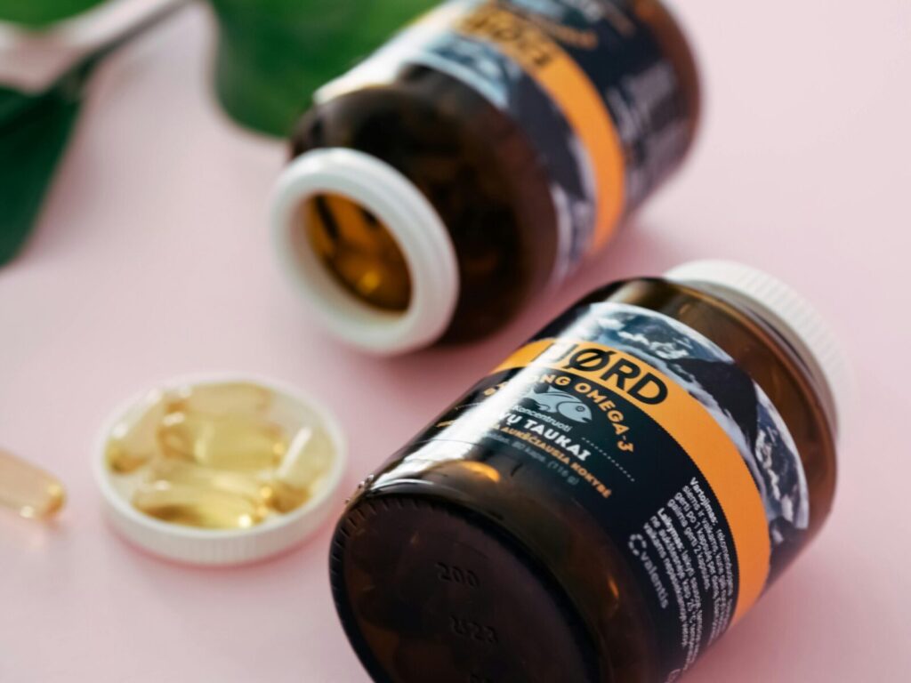 Close-up of Omega-3 fish oil capsules in transparent bottles on a pink background.