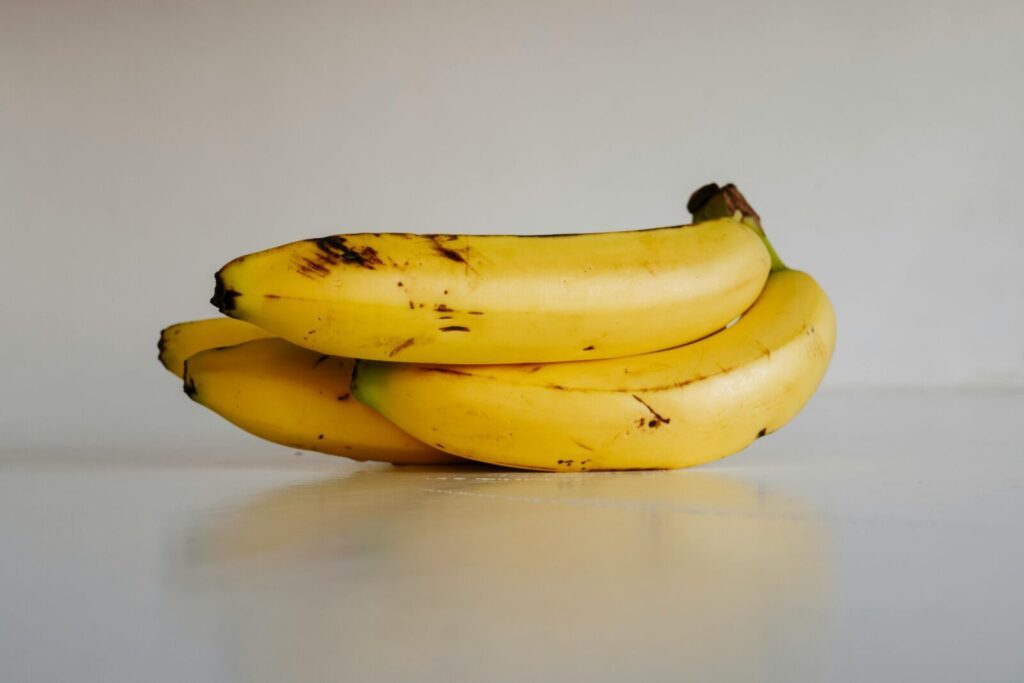 A bunch of fresh yellow bananas stacked elegantly on a smooth white surface, ready to eat.