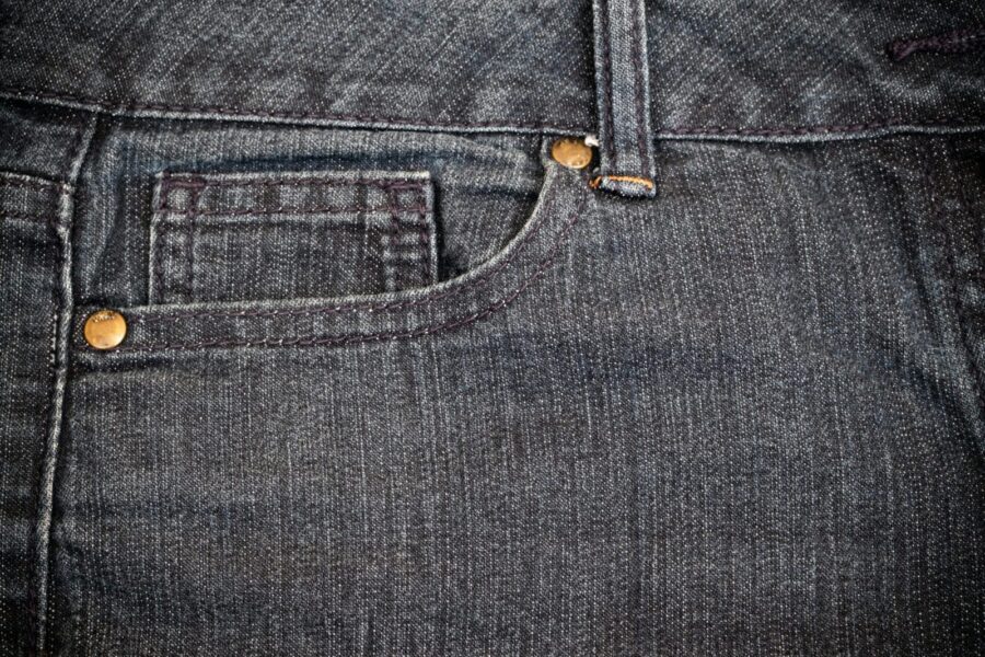 Detailed view of blue denim jeans showcasing stitching and copper rivets.