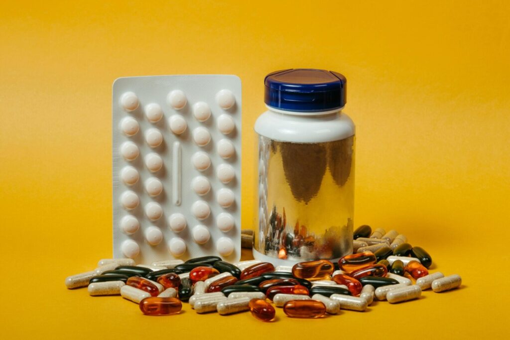 A variety of pills and capsules with a bottle on a vibrant yellow background, ideal for medical themes.