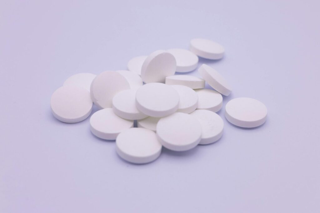 Assorted white tablets stacked on a soft purple surface, symbolizing medication and healthcare.