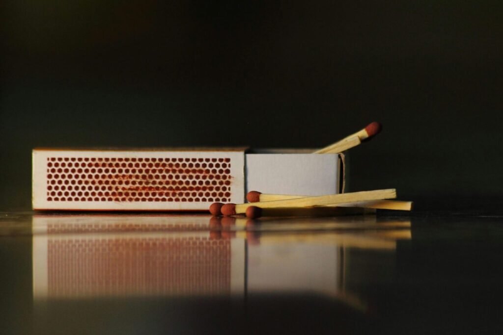 A still life photo of an open matchbox with wooden matches on a reflective surface.