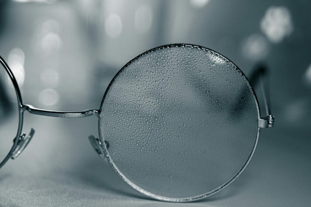 Detailed close-up of eyeglasses with raindrops on lens and gray background.
